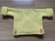 handgestrickte Baby Wickeljacke zartgelb mit orangen Knöpfen